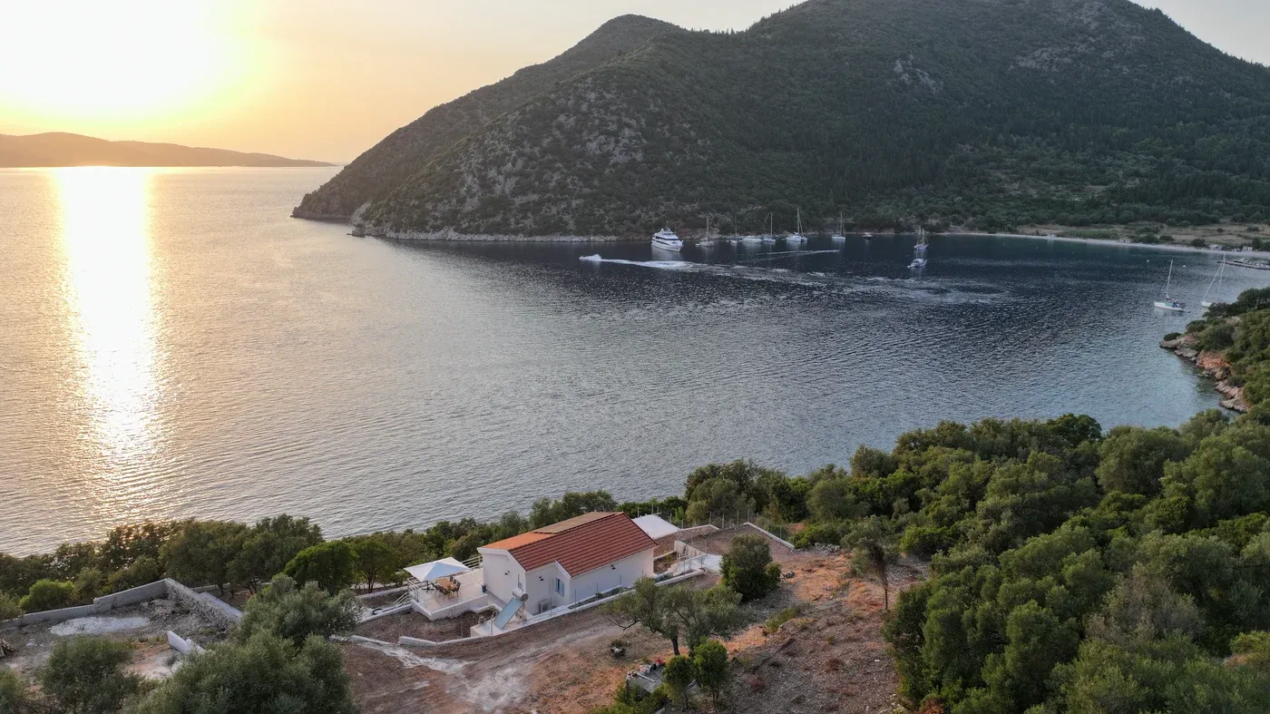Polis bay from the air at sunset, yachts anchored under the headland and the house on the wooded slope below
